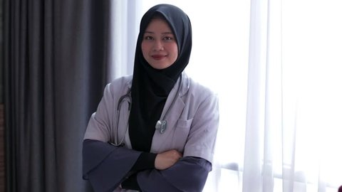 Portrait of asian muslim female doctor standing cross hand and smiling at camera at hospital. Edited and raw.