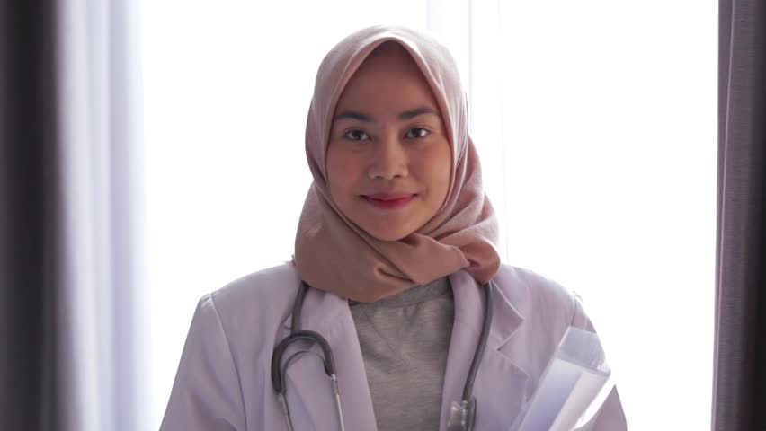 Portrait of asian female muslim doctor standing and smiling at camera at hospital. Edited and raw. Royalty-Free Stock Footage #1014084863