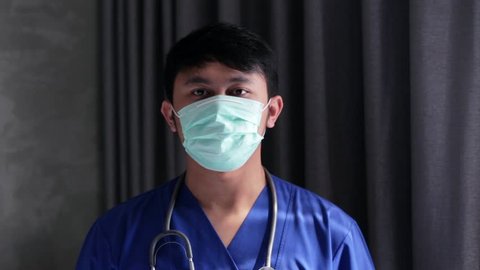 Portrait of asian male doctor puts on medical mask using both hands. Edited and raw.