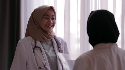 Two asian muslim female doctors have a discussion standing in the hospital together. Edited and raw.