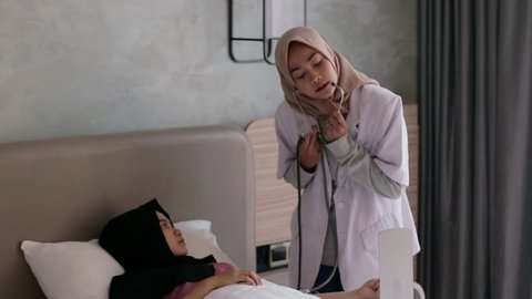Young asian muslim female doctor measuring the blood pressure to patient. Doctor using sphygmomanometer to measure a patients blood pressure. Edited and raw.