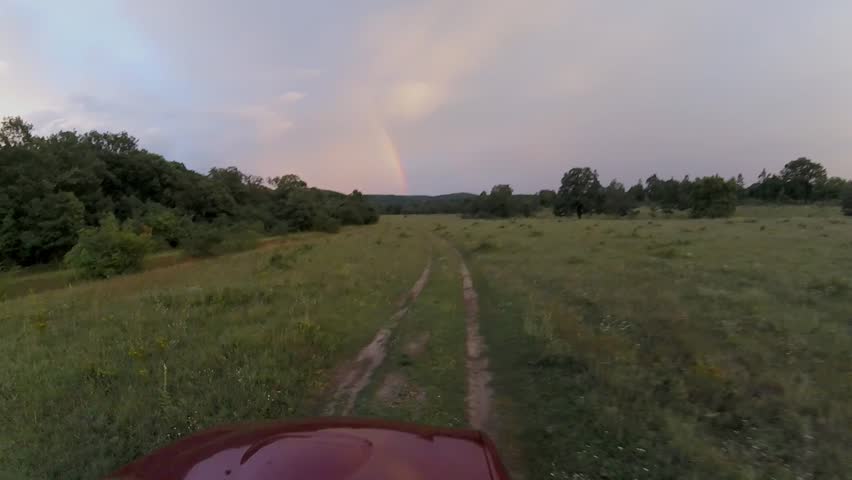 Off road car follow a dirt road towards to rainbow
