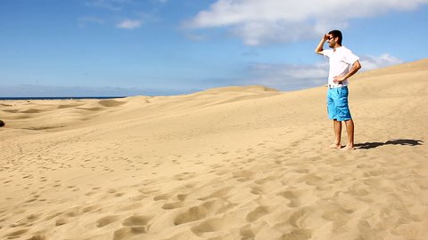 Lost man walks across empty sand dunes desert in Maspalomas, Gran Canaria. Young tourist enjoys wonder views of famous landmark in Canary Islands, Spain. Thirst, adversity, travel destination concepts