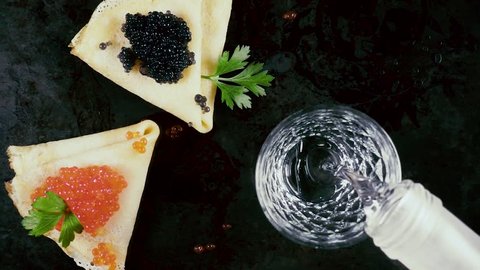 Slow motion pour vodka according to Russian traditions with pancakes with red and black caviar on a dark background top view
