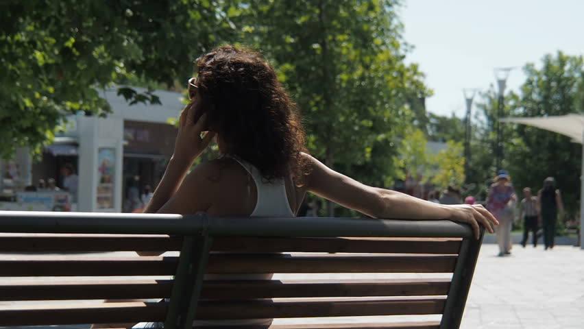 The girl is talking on the phone. Girl on the bench with the phone.