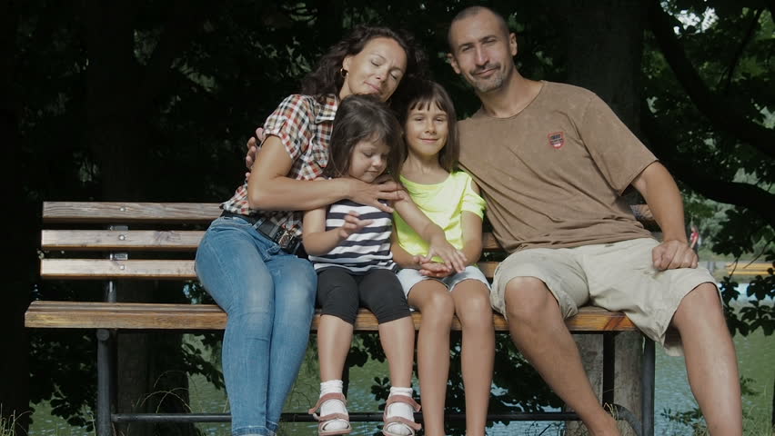 Happy family in the park on the bench. Parents hug children.