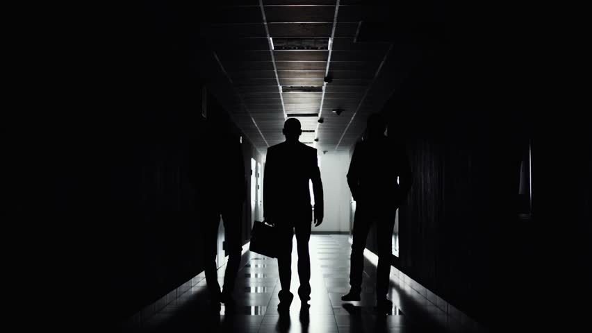 Silhouettes of three businessmen walking in direction of light along the corridor. The end of working day. Team completed the work on project. Businessman go to meeting.  Royalty-Free Stock Footage #1014121580