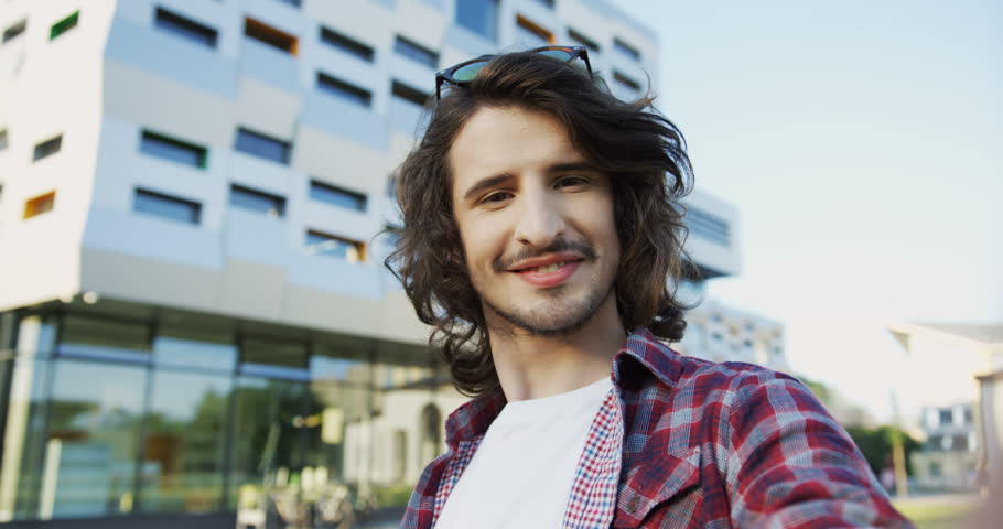 Close up of the young Caucasian man having a videochat on the modern building background and talking. POV. Outside.