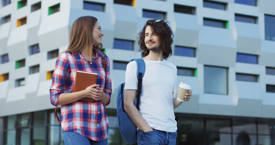 Couple of attractive young man and woman students walking after the lessons with a coffee and talking. Outdoors.