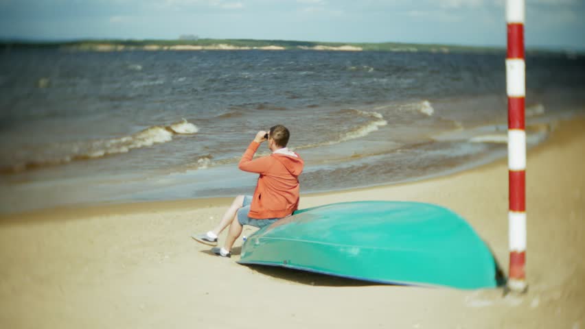 man sits on the beach outside the boat and looks through binoculars 4k