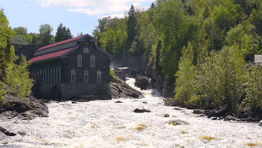 Zooming of La Pulperie de Chicoutimi Regional Museum Pulp mill in Saguenay, Quebec, Canada with river and water current flowing in summer