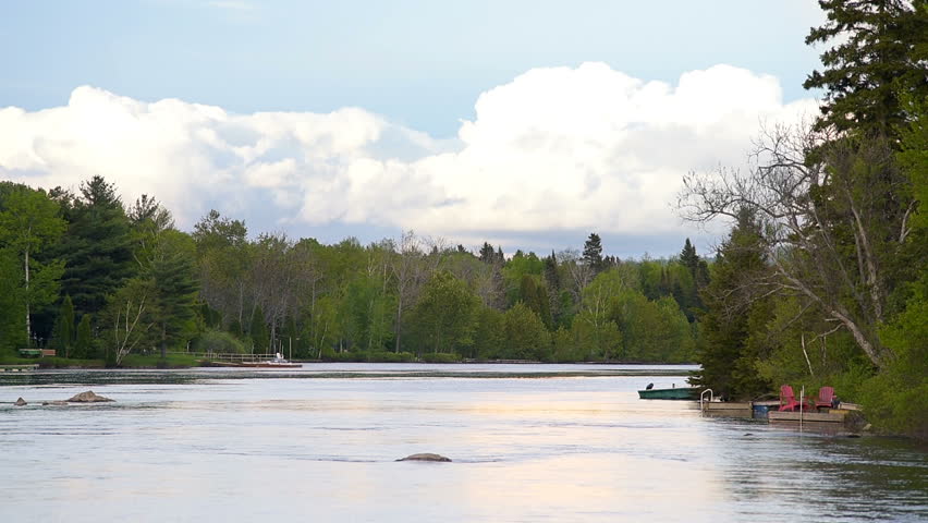 Chicoutimi river in Saguenay, Quebec, Canada with riverfront houses, forest, empty fishing rowboat or motor boat during sunset