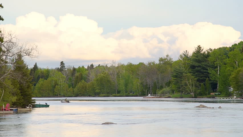 Panning of Chicoutimi river in Saguenay, Quebec, Canada with riverfront houses, forest, man in moving rowboat or motor boat during sunset
