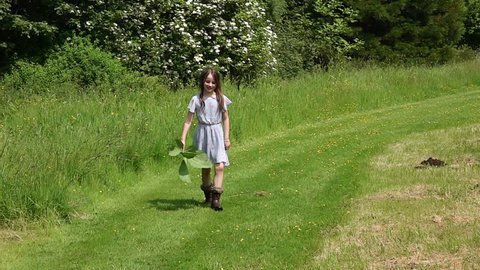 A young girl walks in the countryside in a pretty blue dress. It is summer and the sun shinning