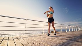 Full length view of Young sports woman in earphones stretching exercise near the sea