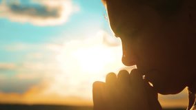 girl praying. girl folded her hands in prayer silhouette at sunset. slow motion video. Girl folded her hands in prayer pray to God. asks forgiveness for sins of lifestyle repentance. believing girl