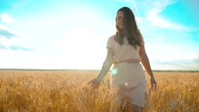 girl is walking along the wheat field nature slow motion video. Beautiful girl in white dress running nature freedom happiness hands to the side on field lifestyle at sunset light and the blue sky