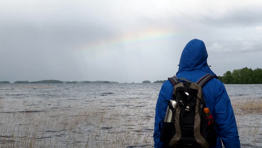 A man looks at a rainbow near water