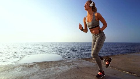 Side view of Concentrated disabled athlete woman in headphones with prosthetic leg running at the beach