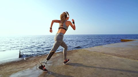 Side view of motivated disabled athlete woman with prosthetic leg running at the beach