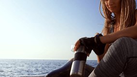 Cropped view of calm disabled athlete woman with prosthetic leg relaxing and drinking water at the beach