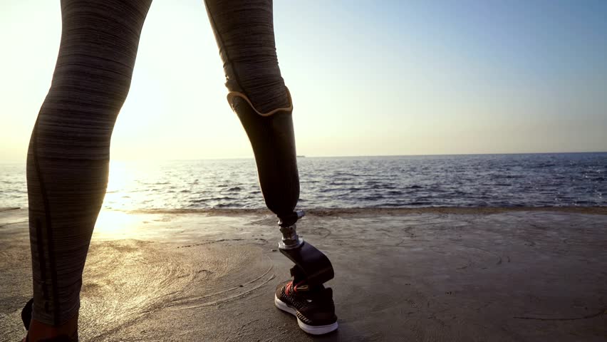 Back view of disabled athlete woman with prosthetic leg warming up at the beach Royalty-Free Stock Footage #1014148184