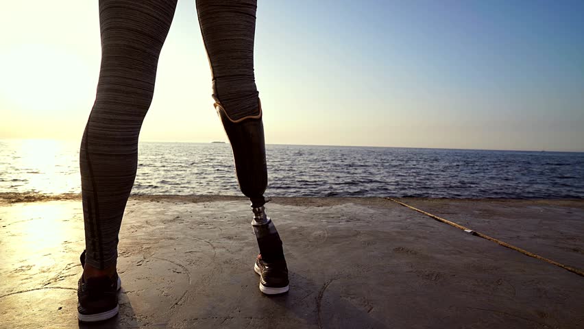 Back view of Concentrated disabled athlete woman with prosthetic leg warming up at the beach Royalty-Free Stock Footage #1014148190