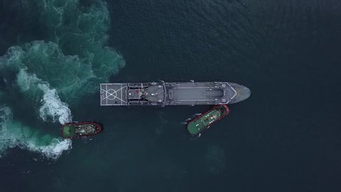 Aerial view of Two Tug Boats assisting a Navy Ship in the Grand Harbour, Malta [Drone Footage]