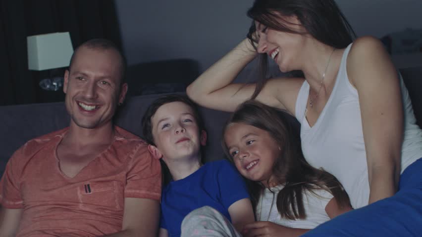 Parents And Their Children Are Watching TV. They Sit On A Sofa In Their Cozy Living Room. It's Evening. Children are fooling and picking up the remote. Royalty-Free Stock Footage #1014155696