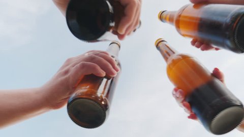 A group of friends clink glasses with beer bottles against the sky, the lower camera angle