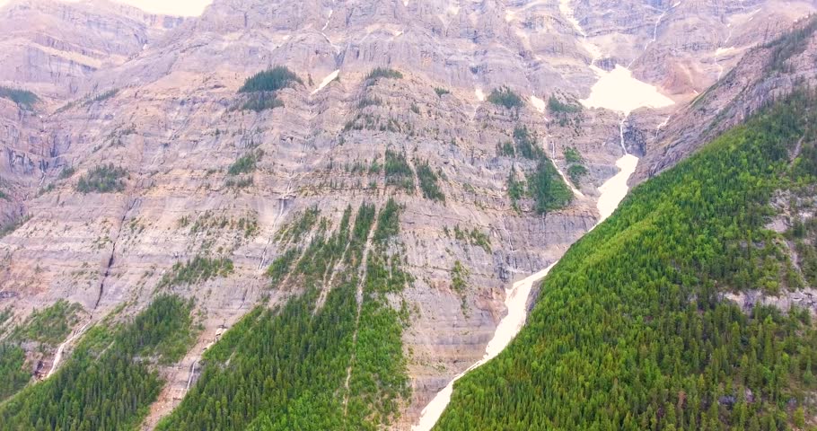 Aerial drone flight over side of mountain in rocky mountains with creeks and waterfalls running down