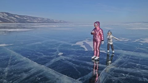 Family is ice skating at day. Girls to ride figure ice skates in nature. Mother and daughter riding together on ice in cracks. Outdoor winter fun for athlete nice winter weather. People on ice skates : vidéo de stock