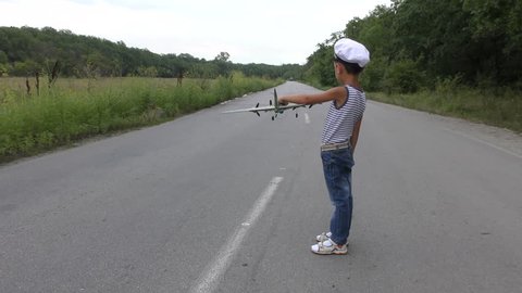 Boy with an airplane in his hands, a runway in the forest. The military plane takes off.