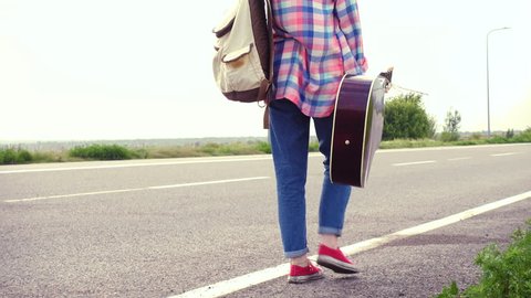 Young girl with a guitar coming along the road and hitch-hiking
