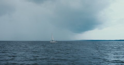 Side view of yacht sailing on a large lake, rainstorm in the background, bad rainy weather. 
