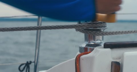 Male turning winch handle on yacht stern adjusting jib while sailing on a large lake, rainstorm in the background, bad rainy weather. 