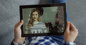 Top view on the black tablet computer in hands of the young woman with beautiful blonde female friend unpacking present near Christmas tree on the screen.