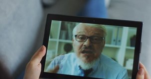 Close up of the black tablet device in hands of the woman with her angry old boss on the screen while they having videochat.