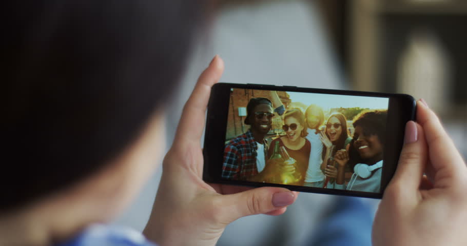 Close up of the black smartphone in hands of the young woman with team of joyful friends on the screen while having videochat. Rear. | Shutterstock HD Video #1014201824