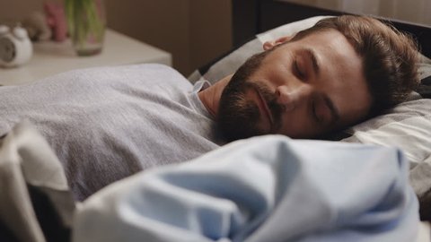 Close up of the handsome man with a beard lying and sleeping in the bed at home. Portrait shot. Indoor