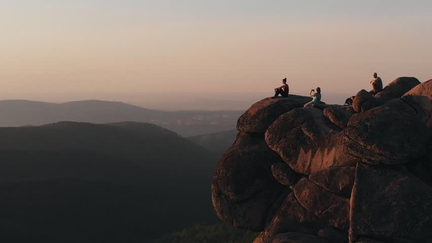 Epic drone shot of friends enjoy the sunset sitting on top of a high mountain in the Siberian Stolby nature reserve. Royalty-Free Stock Footage #1014202313