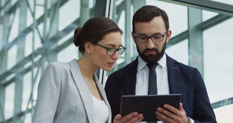 Close up of a handsome businessman in suit and tie showing something about their business on a tablet device screen to a businesswoman and she being surprised.