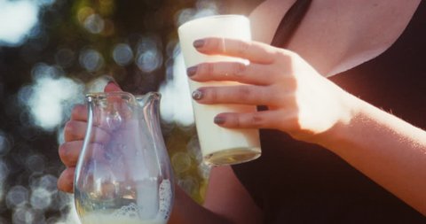 Female hands pour a glass of milk into the jug.