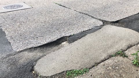 A low angle view of cars passing near a large pothole on a typical American street.  	