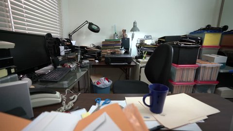Dolly across messy desk in cluttered office with piles of files and coffee cup.