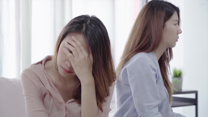 Unhappy Asian lesbian lgbt couple sitting each side of sofa with moody emotion in living room. Women conflict with her girlfriend and have bad relationship at home. | Shutterstock HD Video #1014214835