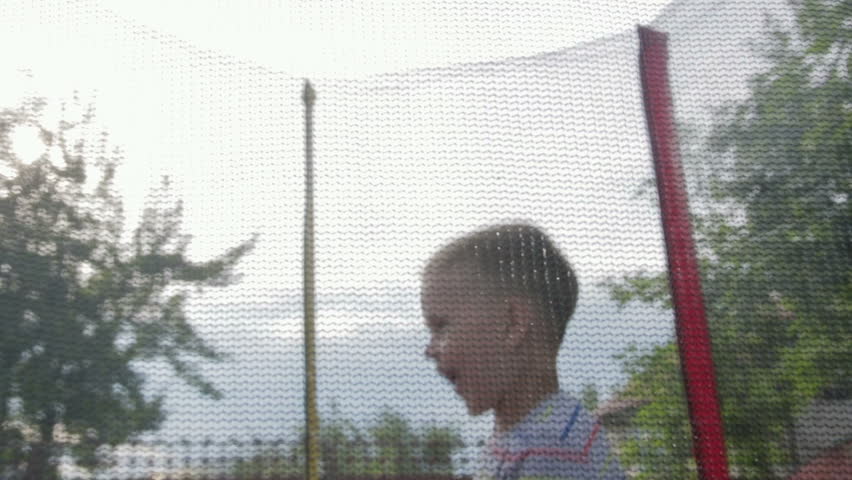 Cheerful, small, happy boy in t-shirt and shorts jumping on a trampoline, trampoline is in the garden