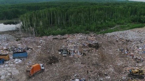 Aerial panoramic view of huge city garbage dump at sunset. Landfill disposal site. Birds fly over piles of trash. Wastes of life and production. Environmental pollution. Garbage truck unloads trash