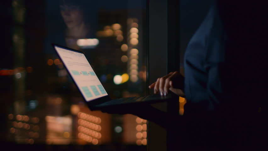 Successful, Stylishly Dressed Businesswoman Holds Laptop While Standing Near the Window of Her Office. Late at Night Professional Woman Doing Important Job.  Shot on RED EPIC-W 8K Helium Cinema Camera