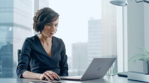 Confident Businesswoman Sitting at Her Desk and Working on a Laptop in Her Modern Office. Stylish Beautiful Woman Doing Important Job.  